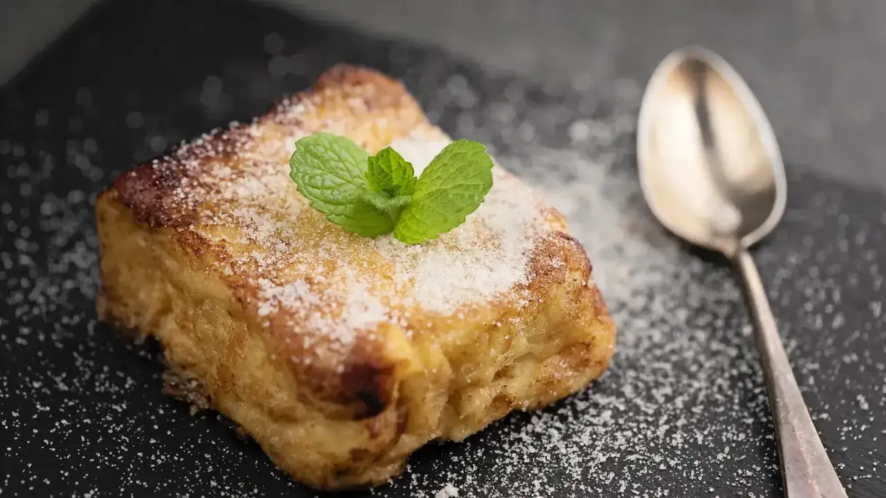 Torrijas con pan brioche, espolvoreadas con az&uacute;car glas y decoradas con menta. Una cuchara plateada descansa a su lado.