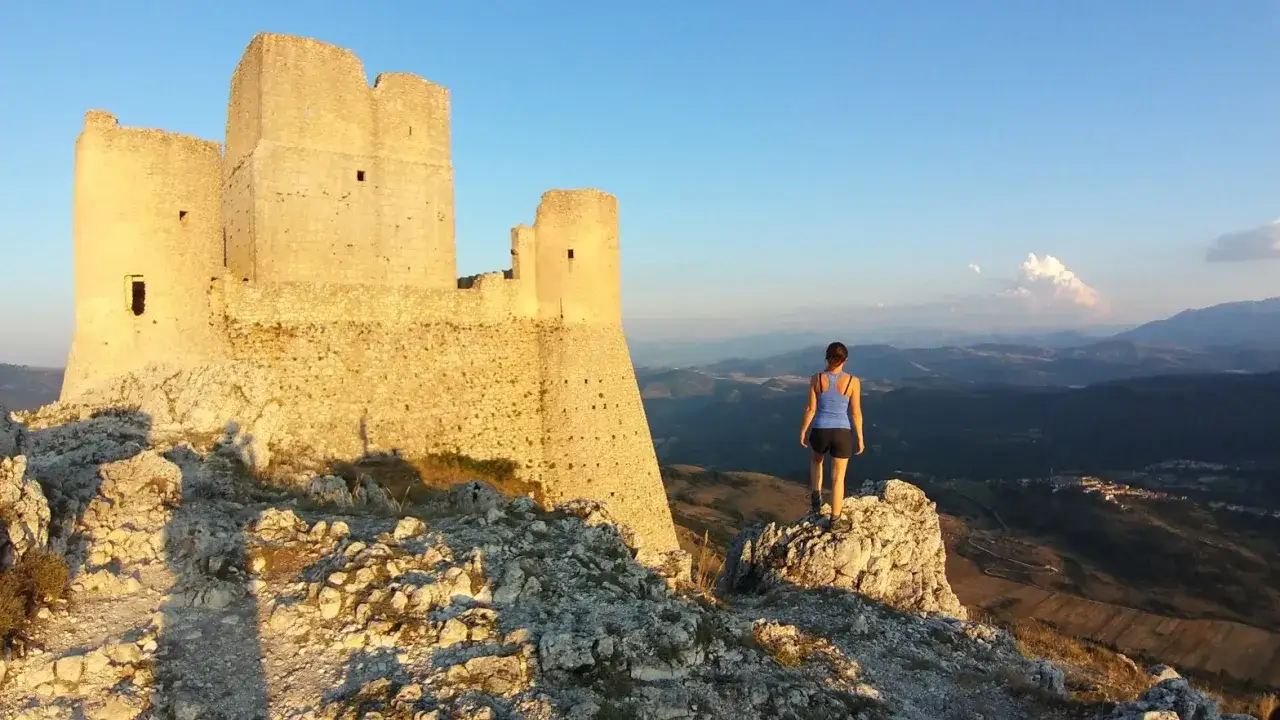 Donna ammira il castello di Rocca Calascio, meta del cammino del Gran Sasso, con vista panoramica sulle montagne.
