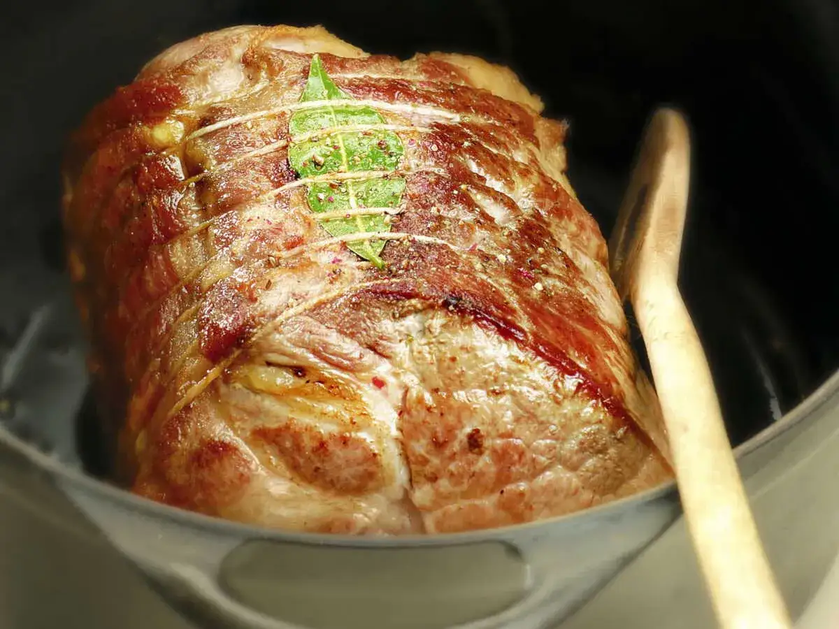R&ocirc;ti de porc ficel&eacute; et garni d'une feuille de laurier, dans une cocotte avec une cuill&egrave;re en bois.