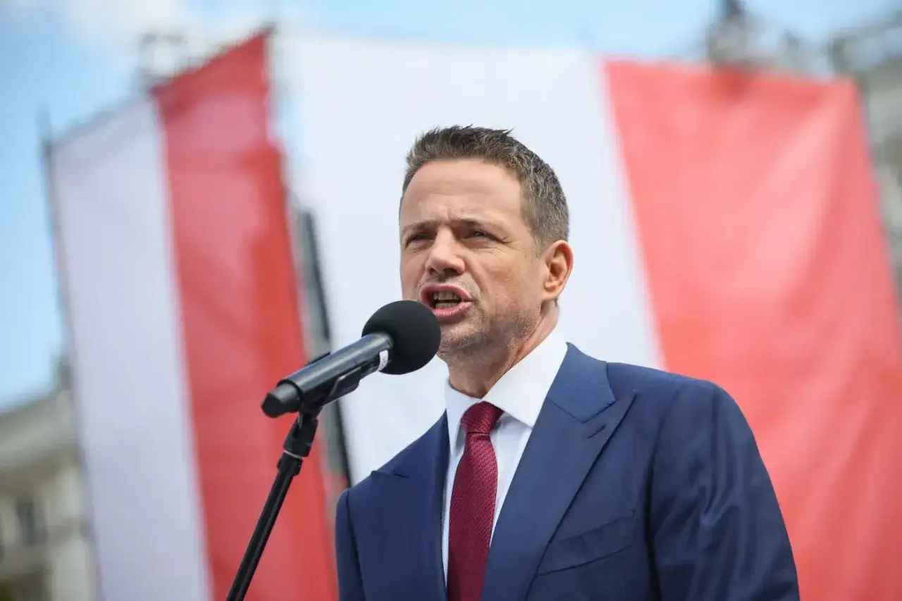 Rafał Trzaskowski, prezydent Warszawy, przemawia na tle biało-czerwonej flagi. Jego życiorys to historia zaangażowania w politykę.