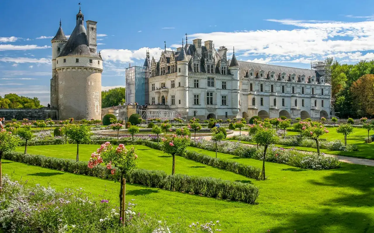 The magnificent Chateau de Chenonceau stands proudly over manicured gardens, its elegant architecture reflected in the clear blue sky.