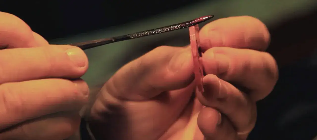 Mani esperte lavorano con precisione su un pezzo di materiale, un dettaglio di attività artigianali che richiede cura e dedizione.