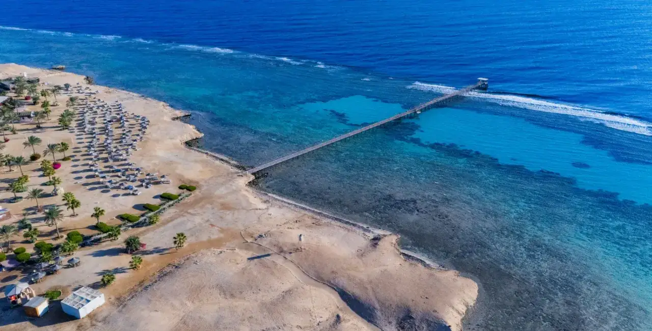 Plaża w Wadi Lahmy Azur z rzędem leżak&oacute;w i palm, długie molo prowadzące na turkusowe morze.