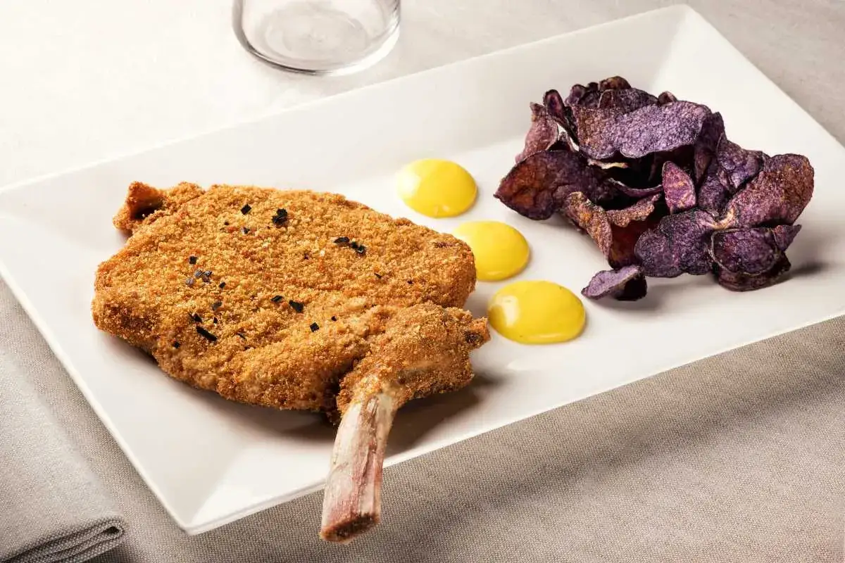 Un crujiente escalope de ternera con hueso, acompa&ntilde;ado de patatas moradas y tres gotas de salsa amarilla.