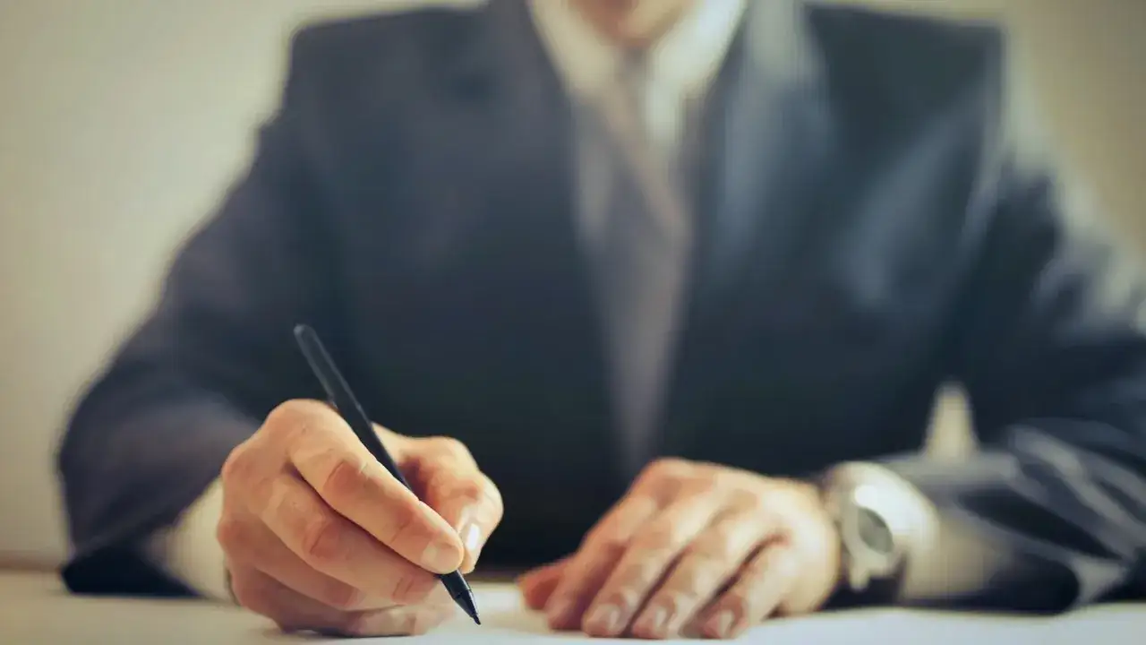 Hombre con traje firmando un contrato con un bolígrafo. Un momento clave para entender como se firma un contrato.