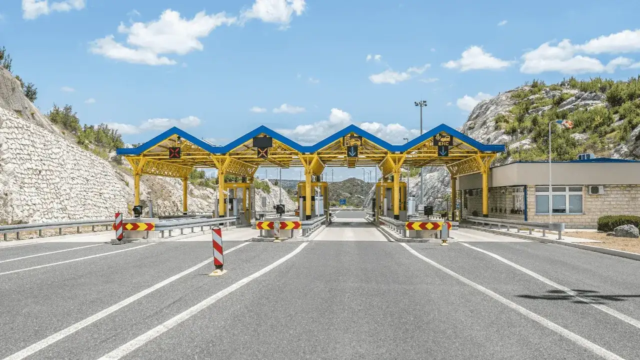Winiety Chorwacja: nowoczesna autostrada z bramkami poboru opłat, otoczona skalistymi wzgórzami pod błękitnym niebem.