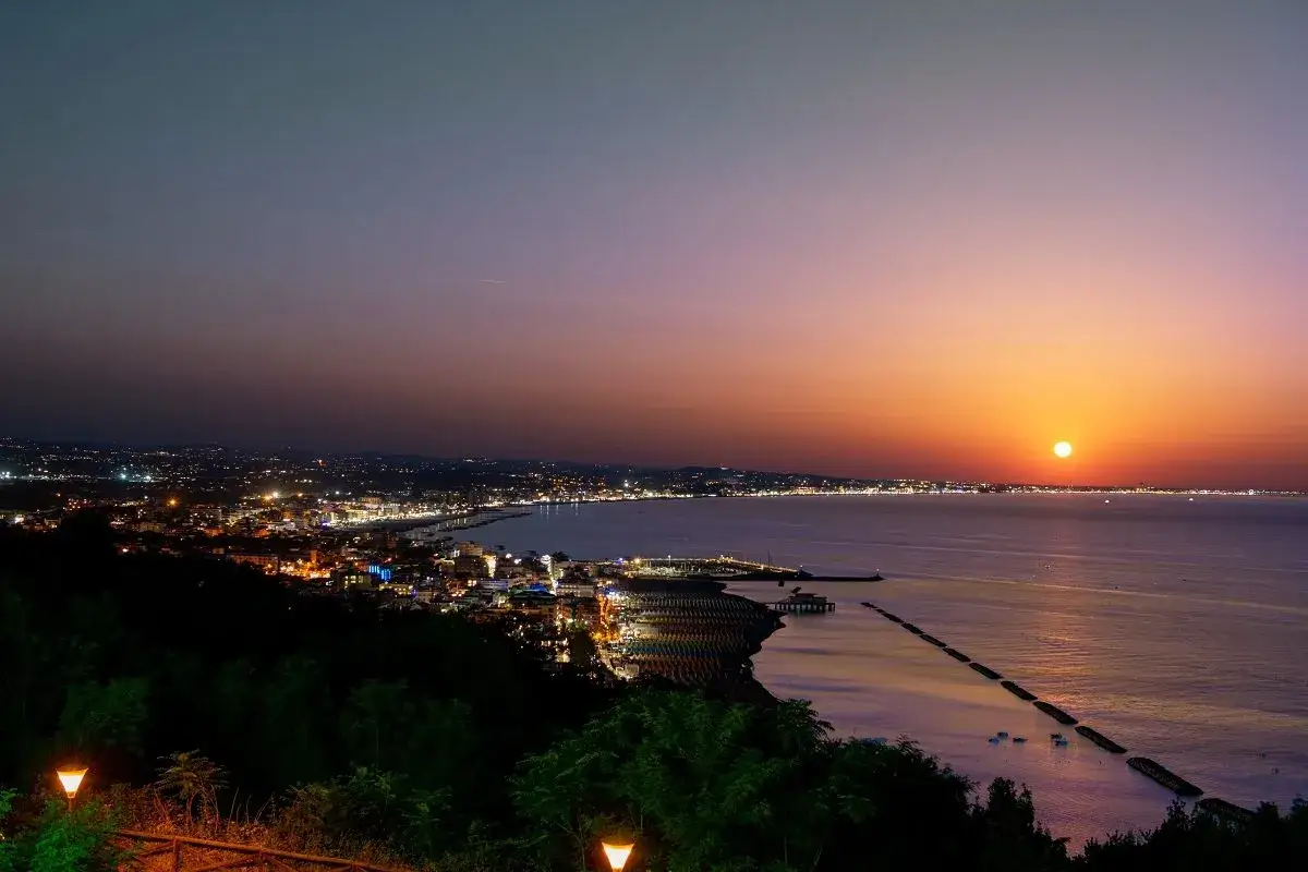 Tramonto sul centro storico e lungomare di Gabicce Mare, con luci accese e mare calmo.