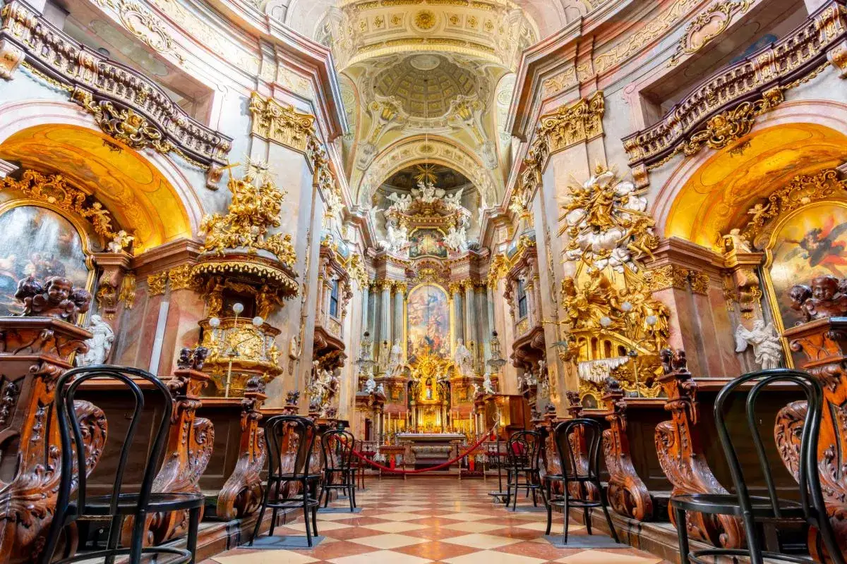 Ornate Baroque church interior, a highlight of 24 hours in Vienna. Golden statues and paintings adorn the walls, with rows of wooden pews leading to the altar.