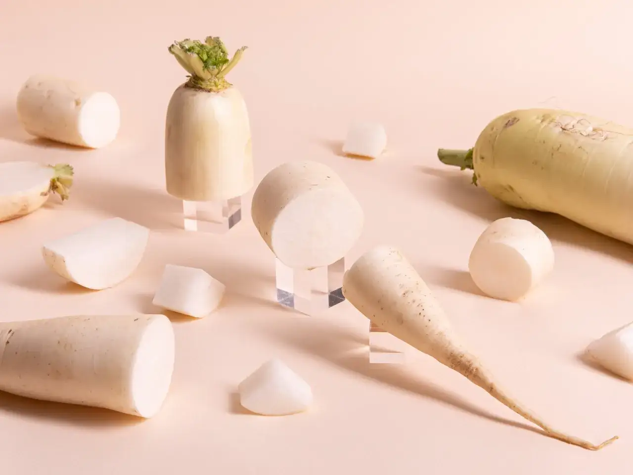 Mehrere daikon rettich Stücke, einige ganz, andere geschnitten, liegen auf einem hellen Untergrund.