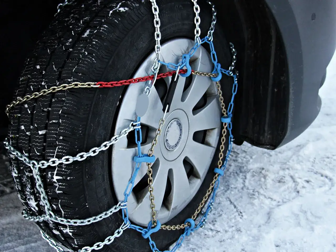 Neum&aacute;tico de coche cubierto de nieve con una cadena del coche instalada para mejorar la tracci&oacute;n en condiciones invernales.