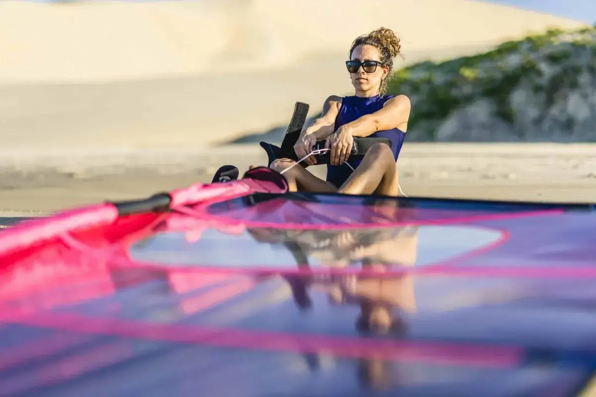 Frau mit Sonnenbrille bereitet sich auf das Windsurfen vor, prüft die Segelleinen. Viele Windsurfen Begriffe sind hier relevant.