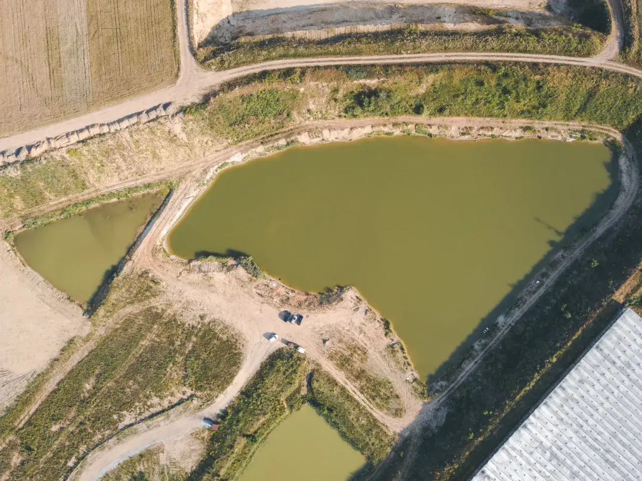 Widok z lotu ptaka na łowisko karp w dolinie. Woda w stawach ma zielonkawy odcień. Wokół stawów widać drogi gruntowe i tereny zielone.