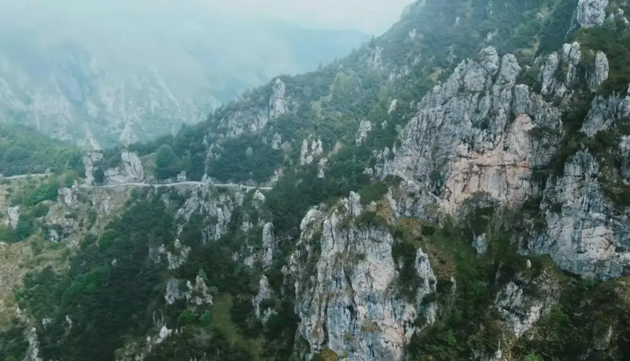 Strada tortuosa che serpeggia tra le rocce scoscese e la vegetazione rigogliosa, un paesaggio mozzafiato che ricorda il passo Barmone.