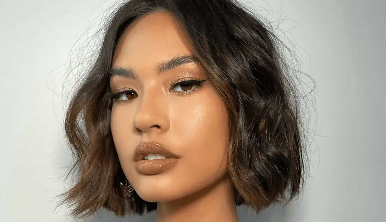 Mujer con melenas cortas con volumen, maquillaje brillante y labios voluminosos.