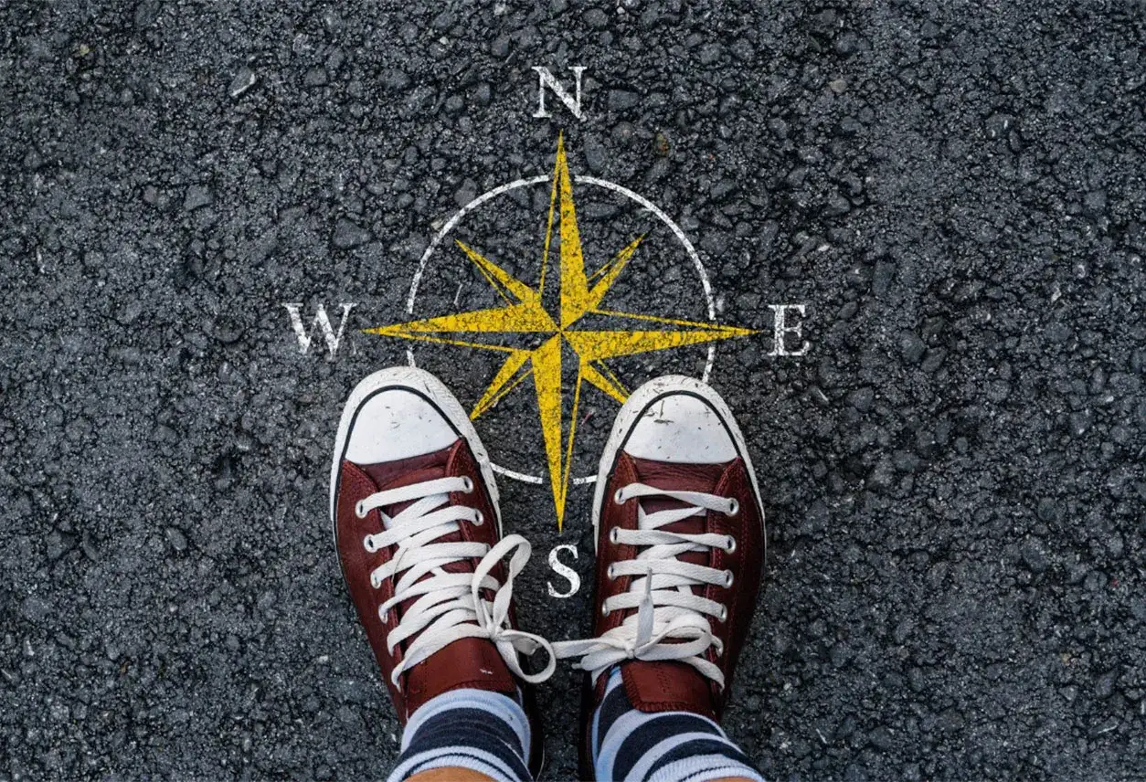 Feet stand on a compass, symbolizing the start of a journey. This image can represent the **mission creep meaning**, where initial goals expand unexpectedly.