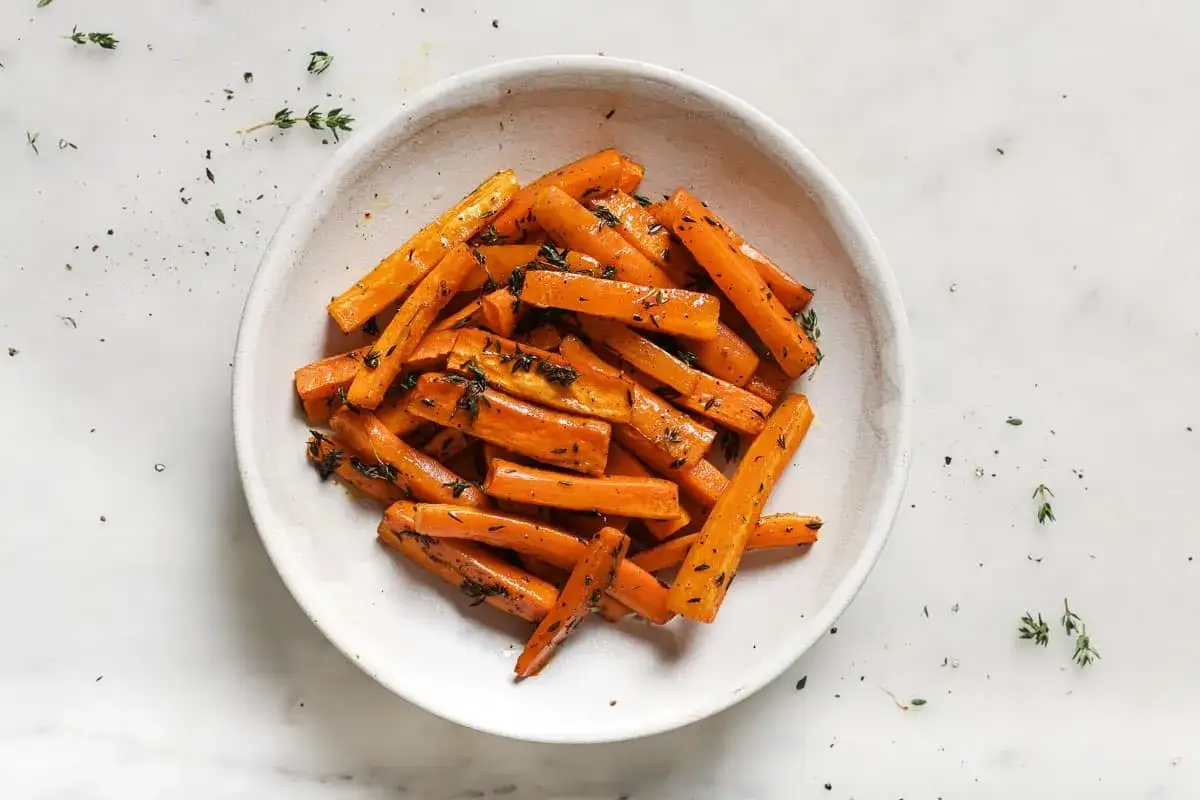 Un plato de zanahorias al horno, cortadas en bastones y espolvoreadas con hierbas frescas.
