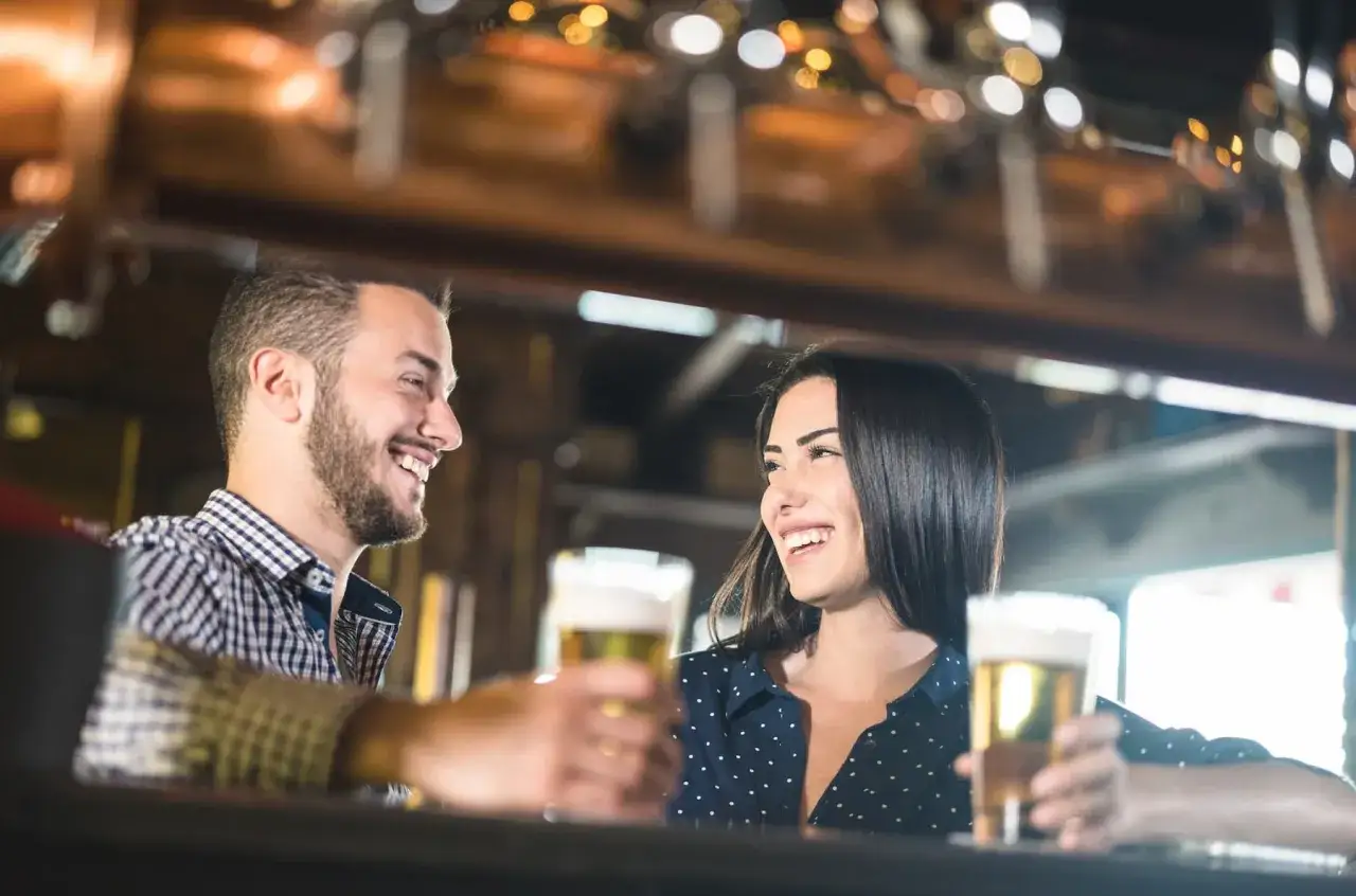 Uśmiechnięta para przy barze, ona pokazuje oznaki flirtu dziewczyny, trzymając piwo.