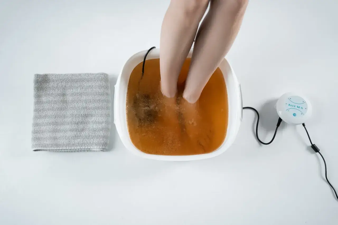 Feet submerged in a foot spa with bubbling, discolored water. A grey towel and a 