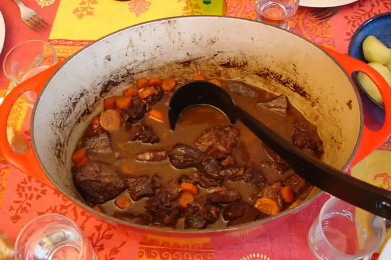 Un plat mijoté de boeuf bourguignon, avec des morceaux de viande tendres et des carottes, servi dans une cocotte orange.