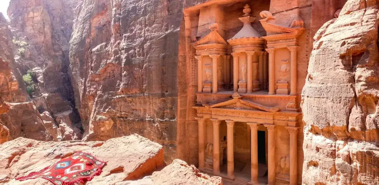 En färggrann matta ligger utbredd på klipporna framför den imponerande fasaden av Al-Khazneh, en av de mest kända sevärdheterna i Petra, Jordanien.