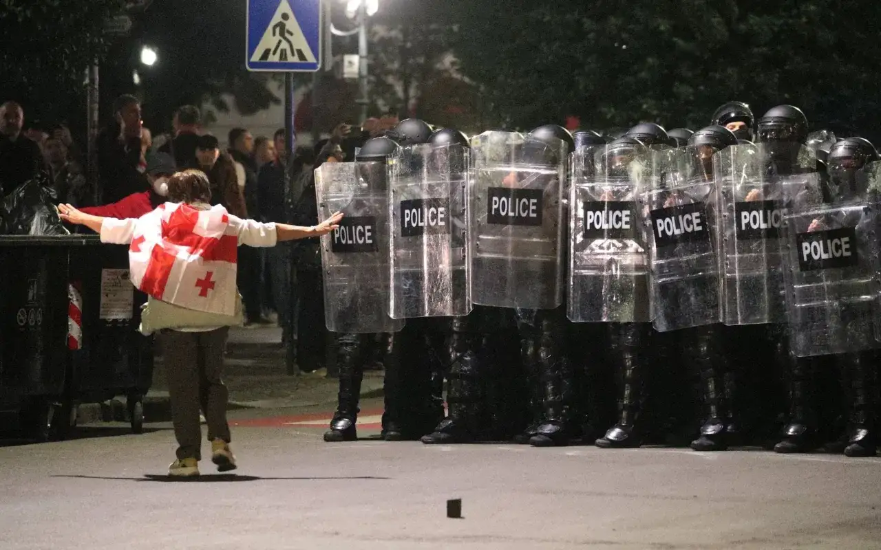 Osoba z flagą Gruzji staje naprzeciw policji w transparentach. Sytuacja polityczna w Gruzji napięta.