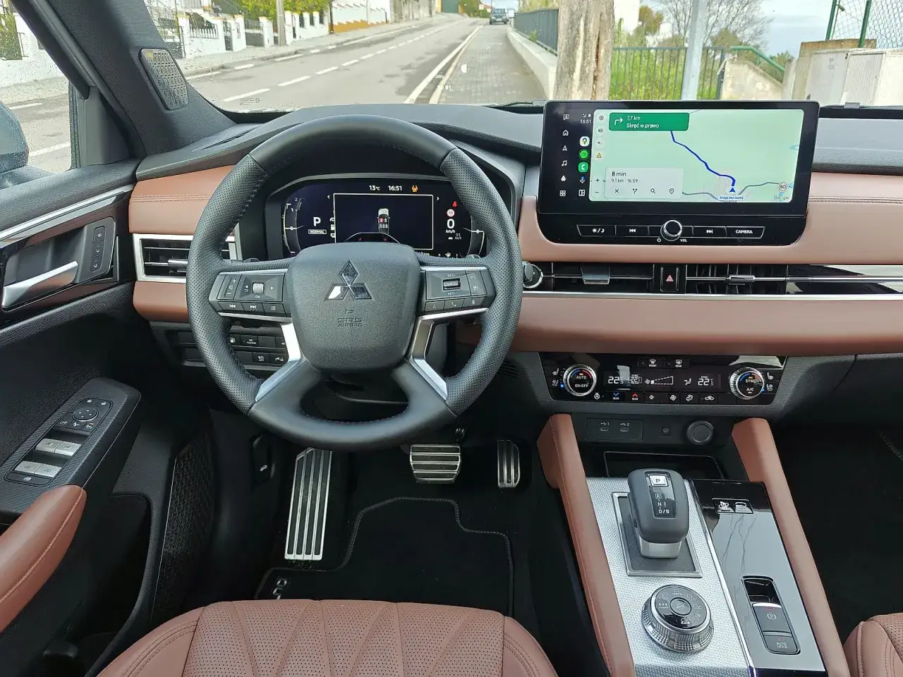 Wnętrze Mitsubishi Outlander 2025 z brązową skórzaną tapicerką, dużym ekranem multimedialnym z nawigacją i cyfrowym kokpitem.