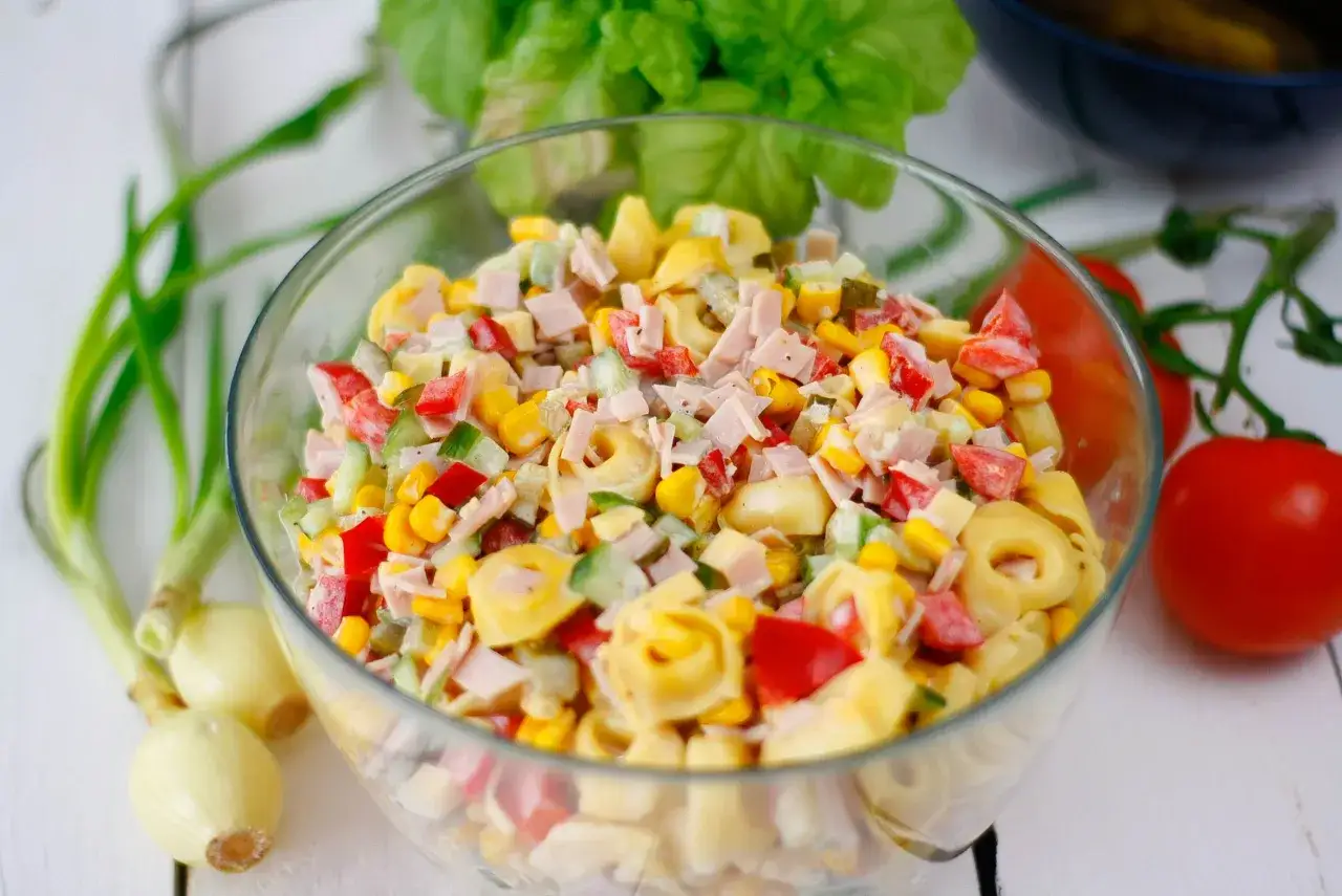 Kolorowa, najlepsza sałatka z tortellini z szynką, kukurydzą, papryką i ogórkiem w szklanej misie.