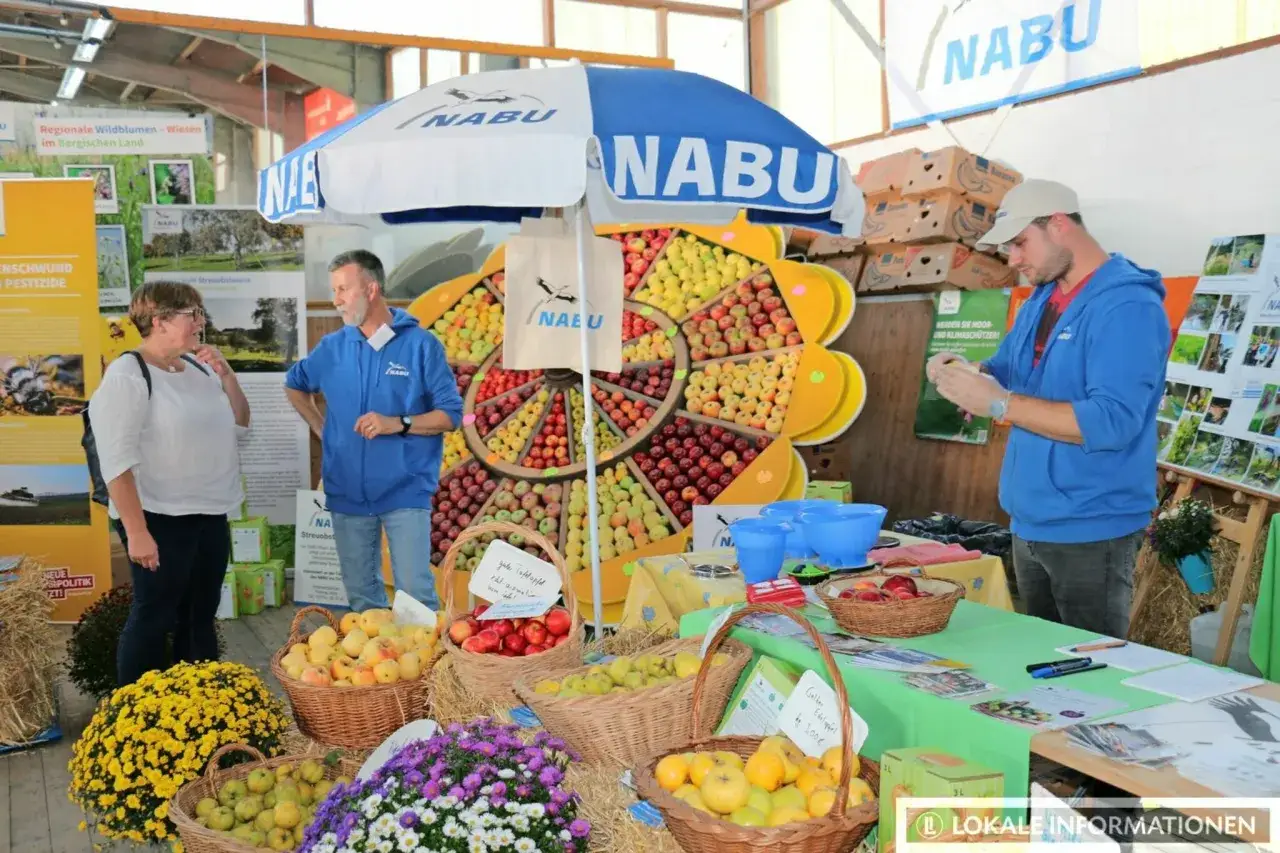 Auf dem Markt Leichlingen pr&auml;sentiert der NABU &Auml;pfel und Blumen. Ein Mann und eine Frau stehen an einem Stand mit vielen Fr&uuml;chten.