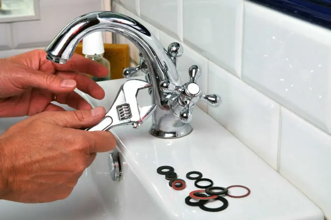 Mains tenant une cl&eacute; pour changer un joint de robinet. Des joints sont pos&eacute;s sur le lavabo.