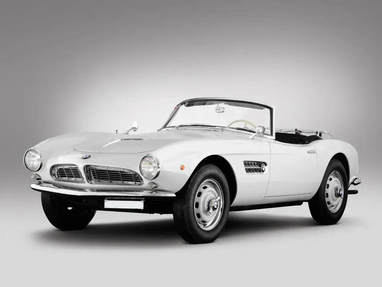 Biały kabriolet BMW 507 z lat 50. na tle szarego tła, klasyk motoryzacji.