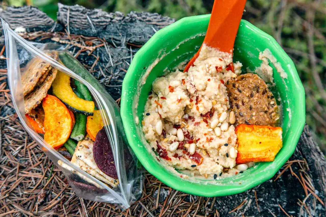 Un d&eacute;licieux repas randonn&eacute;e : houmous &eacute;pic&eacute; avec des crackers et des l&eacute;gumes s&eacute;ch&eacute;s dans un sac. Parfait pour reprendre des forces en pleine nature.