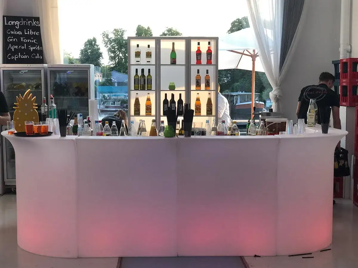 Leuchtender Tresen mit vielen Flaschen, bereit für Cocktails mit Gin. Ein Ananas-Dekor und Gläser mit Getränken stehen bereit.