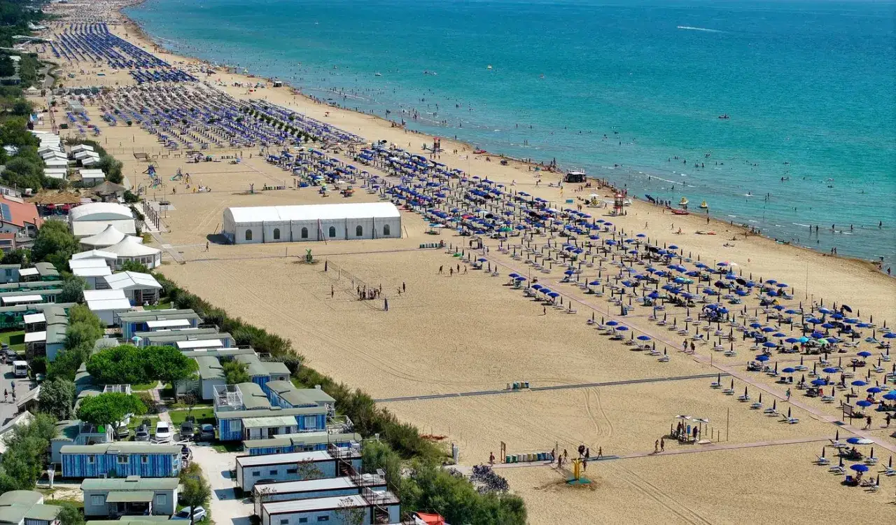 Słoneczna plaża w Capalonga z rzędami leżaków i parasoli, w tle widać morze i zabudowania kempingowe.