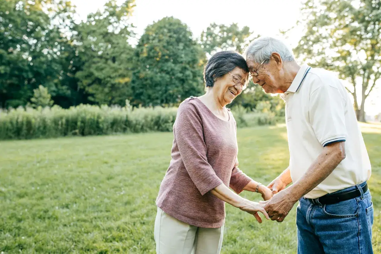 Un couple &acirc;g&eacute; se tient la main, front contre front, dans un parc. Leur sourire et leur proximit&eacute; montrent comment prouver son amour, m&ecirc;me apr&egrave;s des ann&eacute;es.