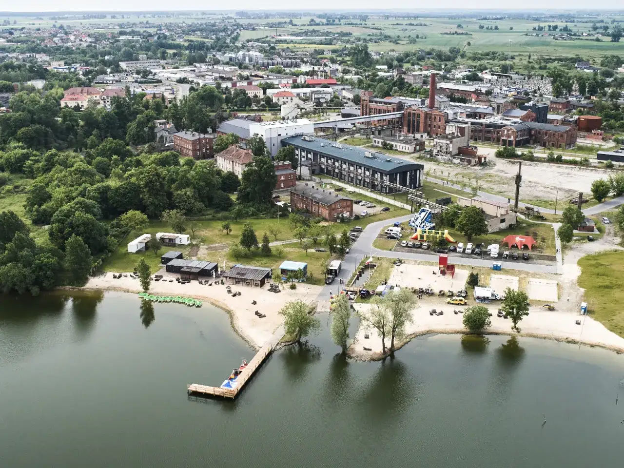 Żnin atrakcje dla dzieci: plaża, wodny plac zabaw i molo nad jeziorem. W tle zabudowania miejskie i tereny zielone.