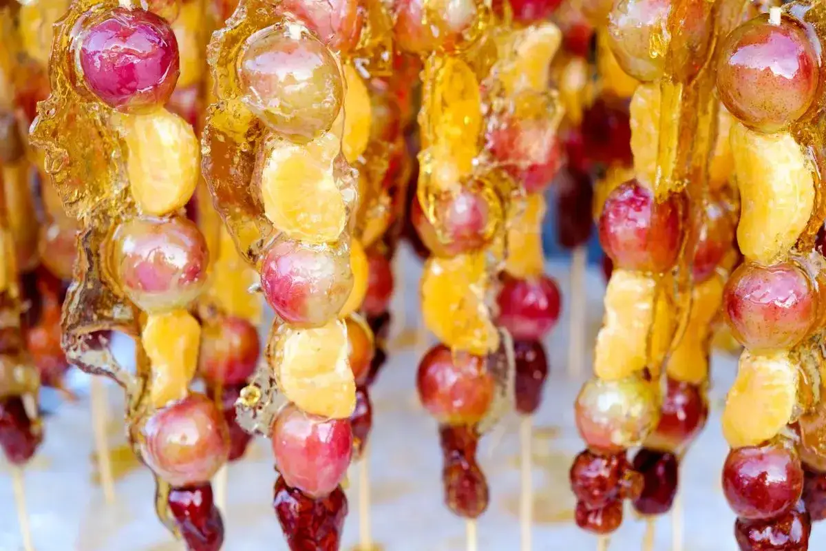 Spiedini di frutta caramellata con acqua e zucchero, un dolce croccante e succoso.