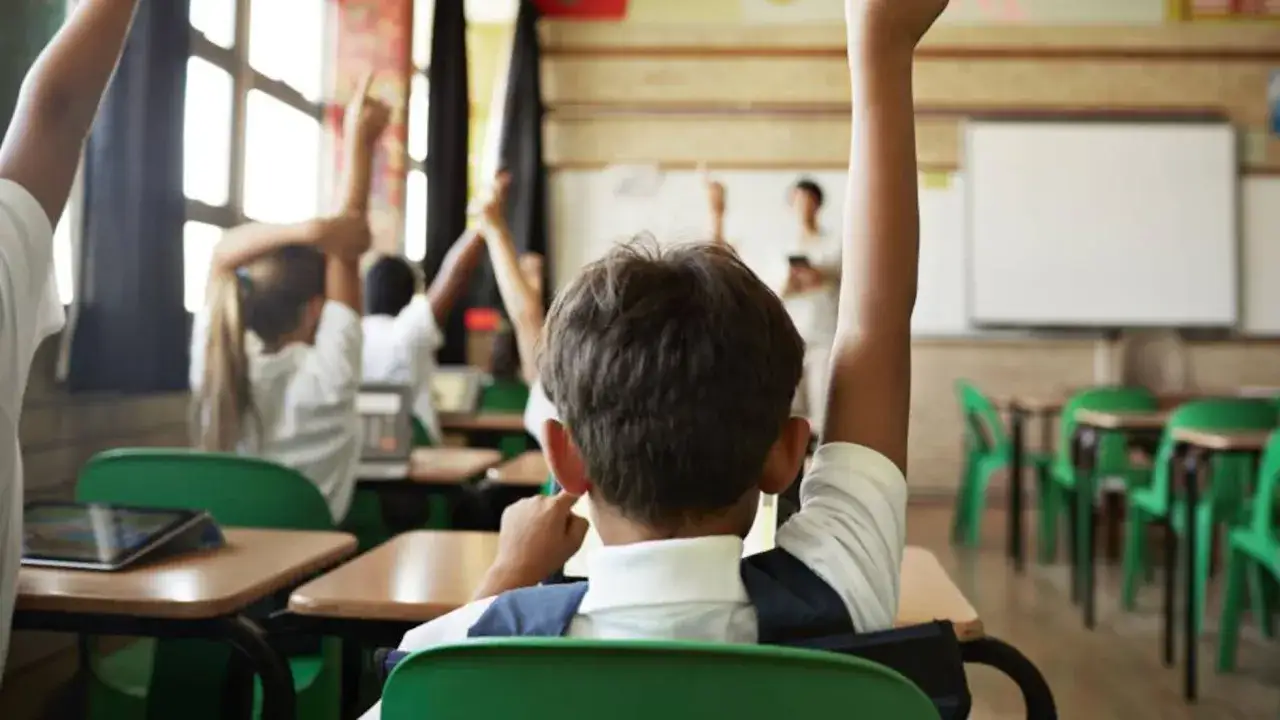 Niños en clase, uno con asperger, levantan la mano con entusiasmo.