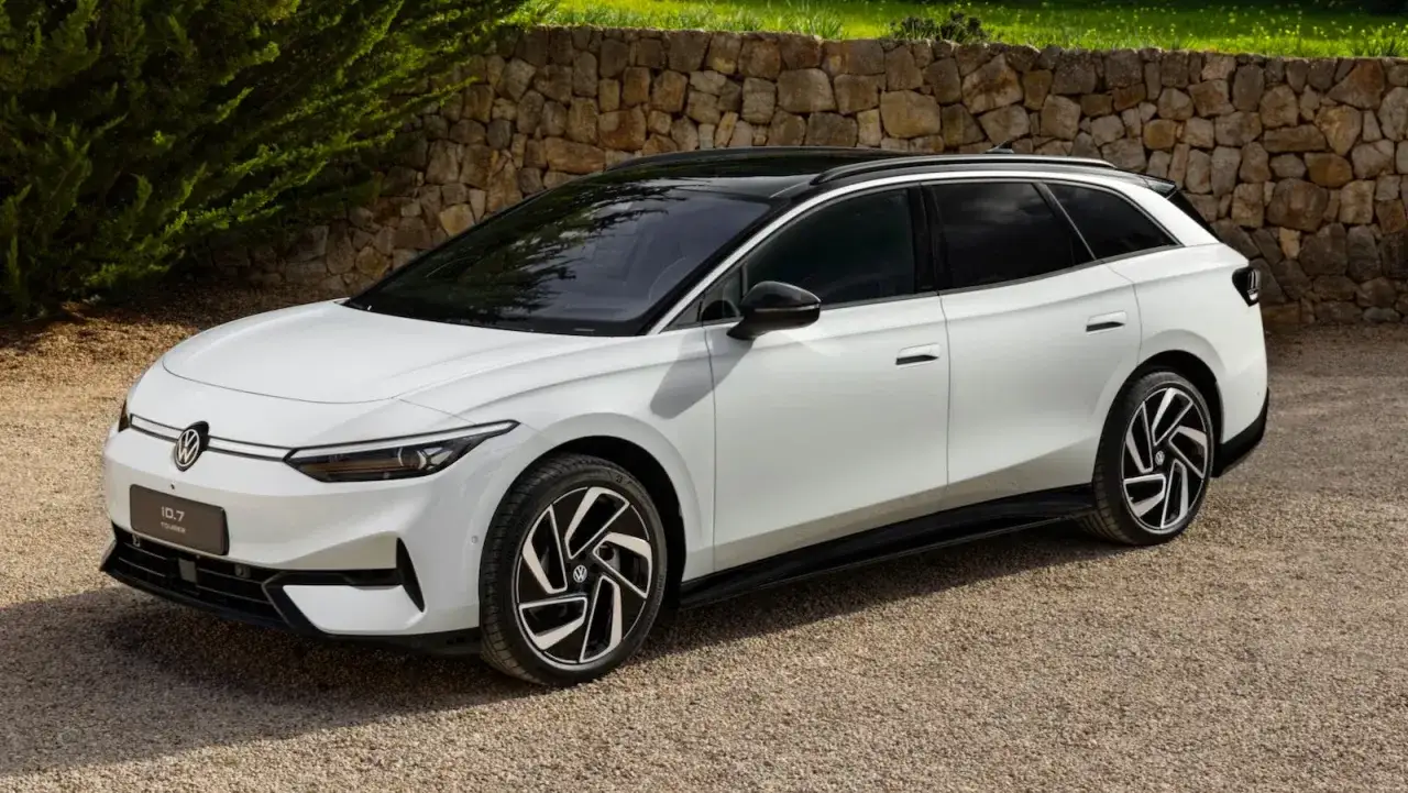 Un elegante coche eléctrico grande blanco, el Volkswagen ID.7 Tourer, descansa sobre grava frente a un muro de piedra.