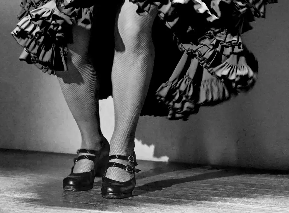 Taconeo flamenco: pies con medias de rejilla y zapatos de baile golpean el suelo, la falda ondea.