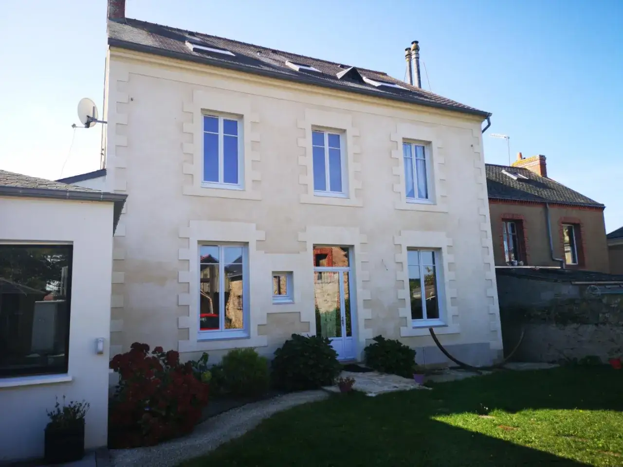 Belle maison en pierre calcaire avec des fenêtres bleues et un jardin verdoyant.