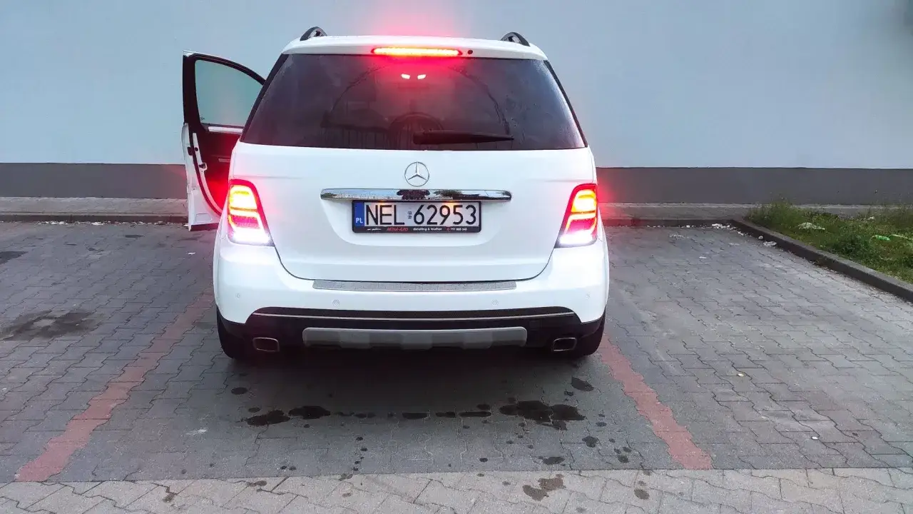 Biały Mercedes z otwartymi drzwiami, światła stopu świecą. Na tablicy rejestracyjnej NEL 62953.