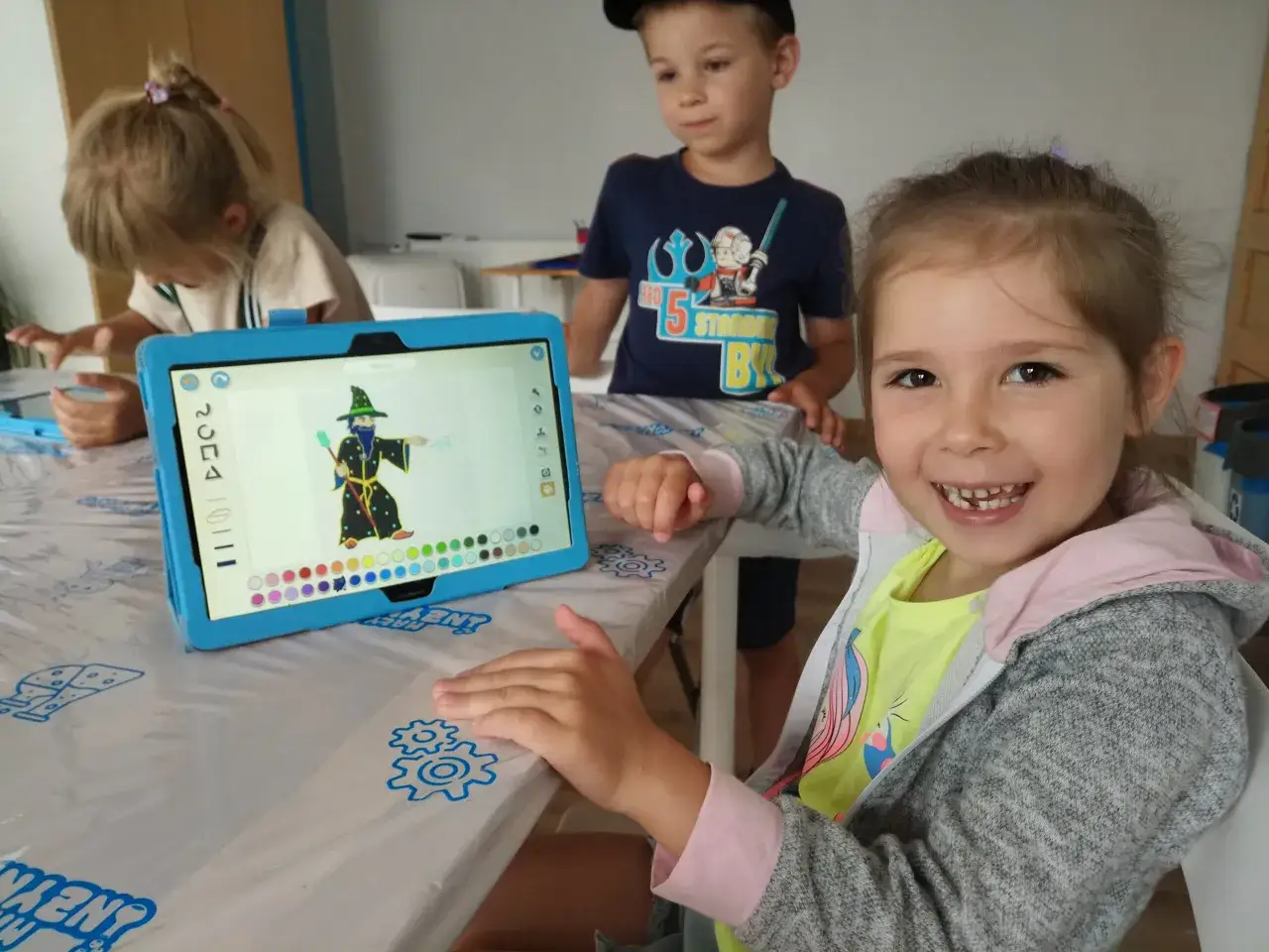 Uśmiechnięta dziewczynka z tabletem, na którym widnieje kolorowanka czarodzieja. To świetny przykład kodowania dla dzieci, rozwijający kreatywność.