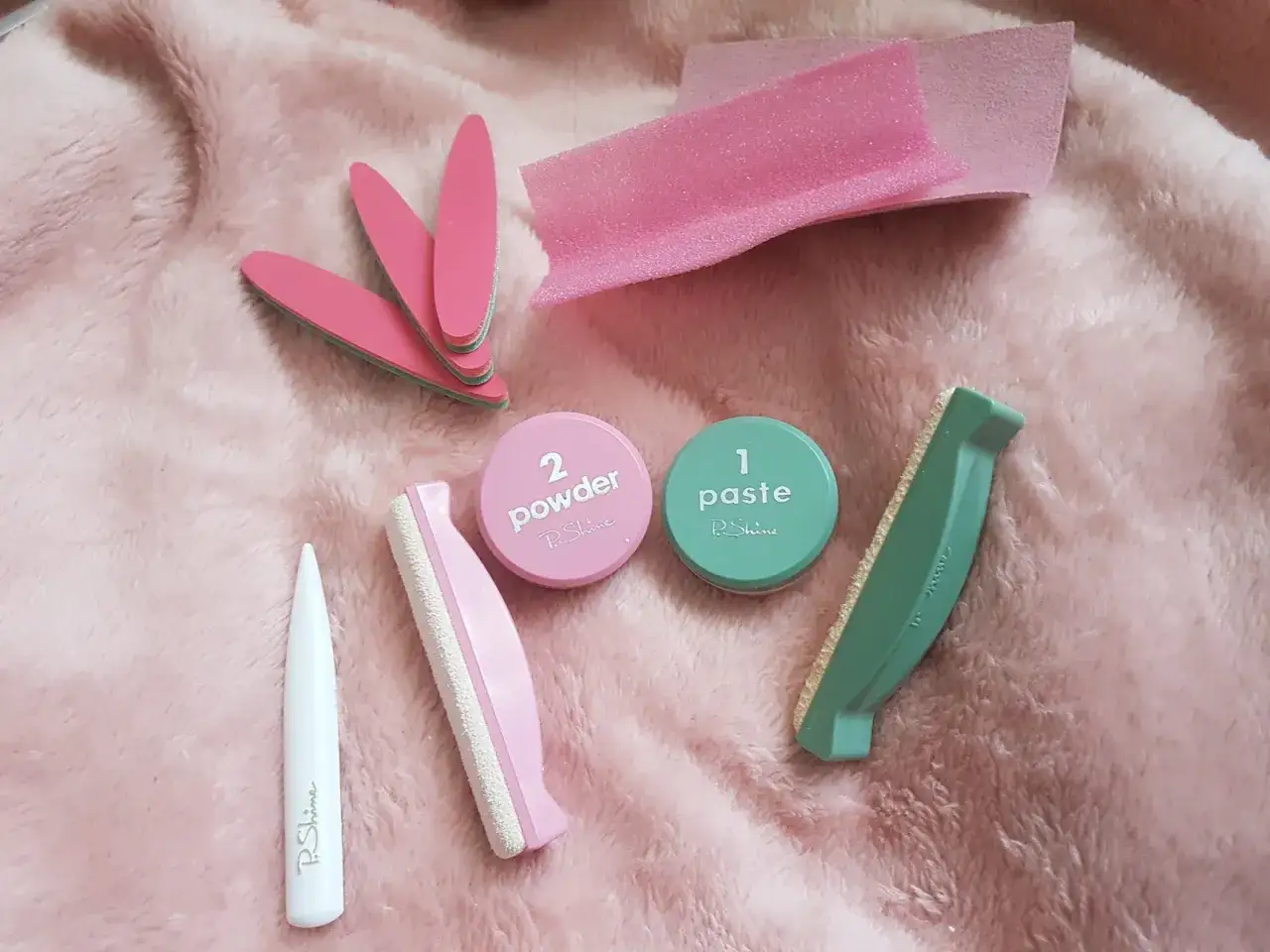 Zestaw do japońskiego manicure: pilniczki, puder, pasta i polerki na różowym, puszystym tle.