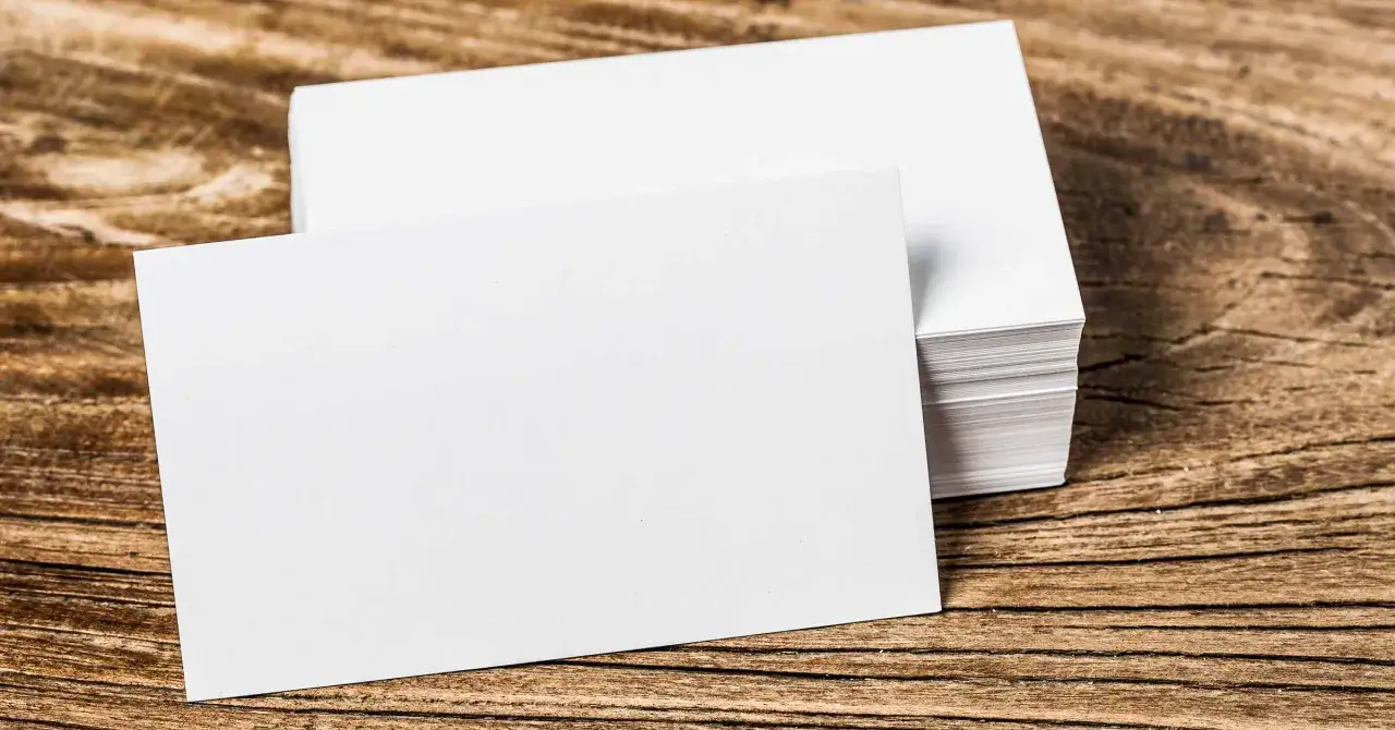 Pila de tarjetas de visita blancas sobre madera. El gramaje del papel es ideal para impresión profesional.