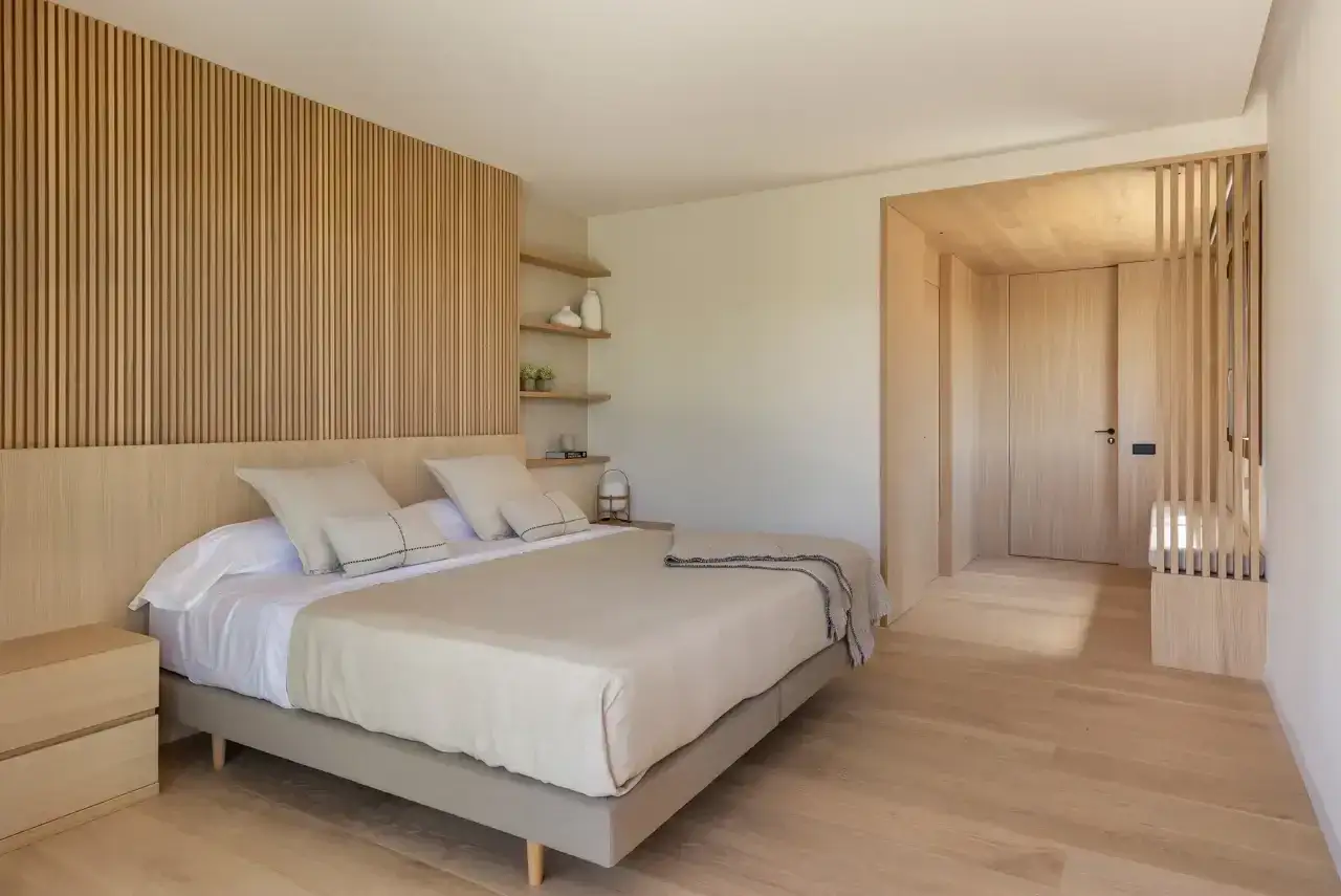 Dormitorio con decoración minimalista. Pared de lamas de madera, cama beige y suelo de parqué claro.