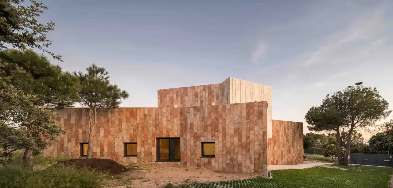 Fachadas exteriores de casas modernas con revestimiento de piedra natural, integradas en un paisaje con árboles y cielo despejado.
