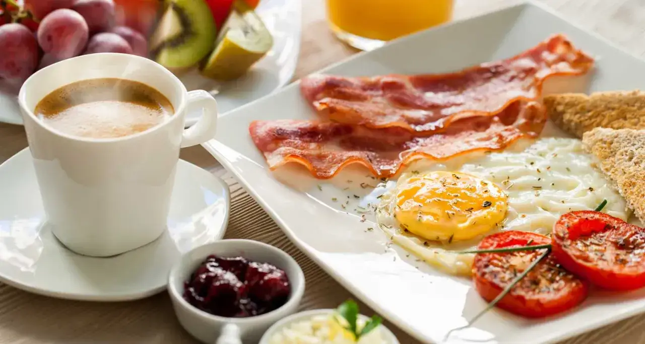 Herzhafter Fr&uuml;hst&uuml;cksteller mit Spiegelei, Speck, Toast, Tomaten und einer Tasse dampfenden Kaffee. Ein guter Start in den Tag, der Energie und Magnesium liefert.