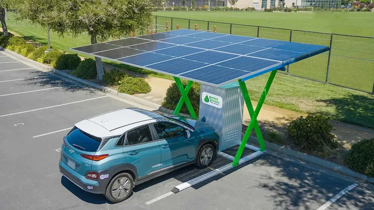 Coche el&eacute;ctrico azul cargando bajo una estructura con placas solares. Energ&iacute;a limpia para cargar tu coche el&eacute;ctrico en casa.