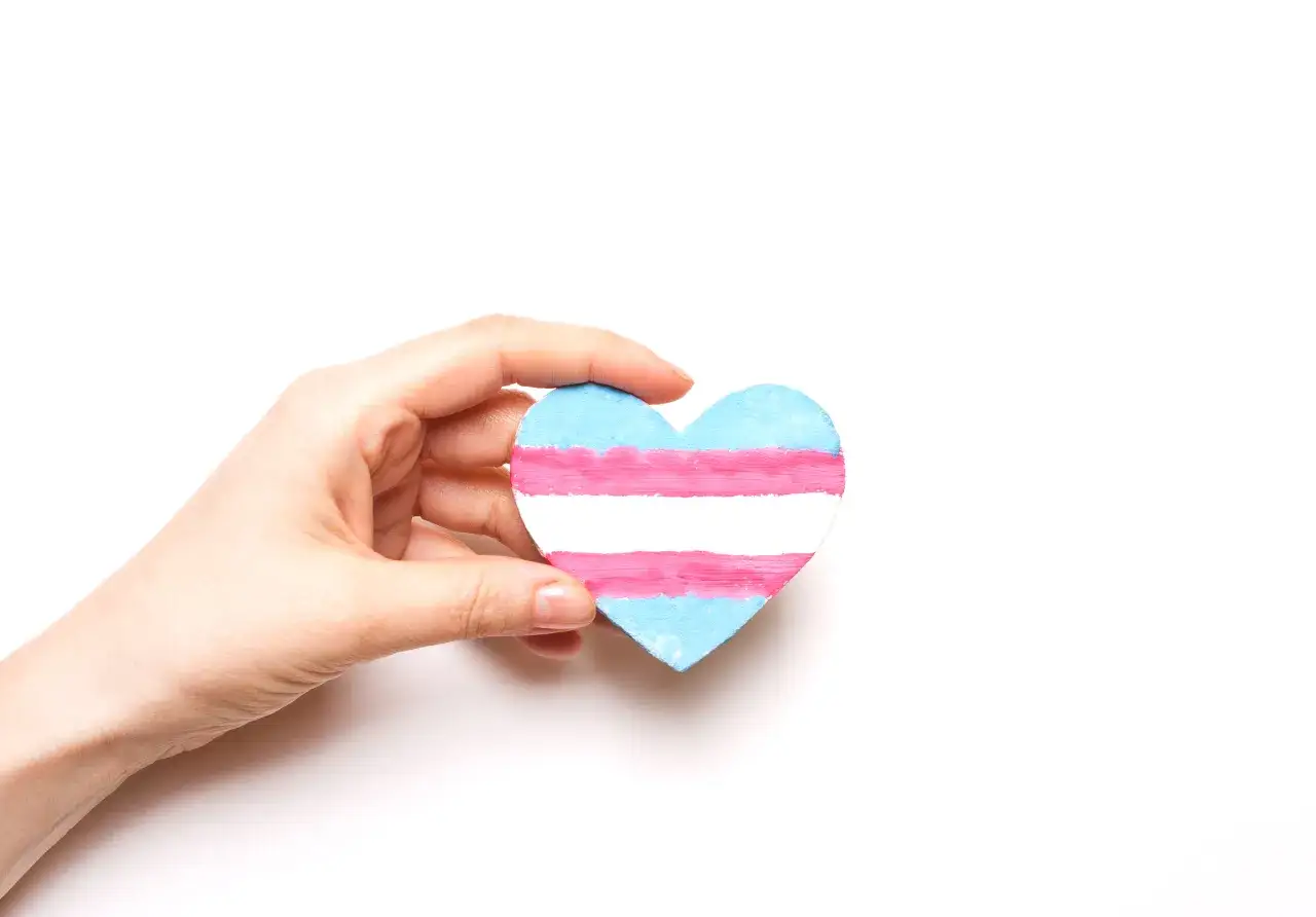 Dłoń trzyma serce z flagą transpłciowości. To symbol tego, czym jest transpłciowość.