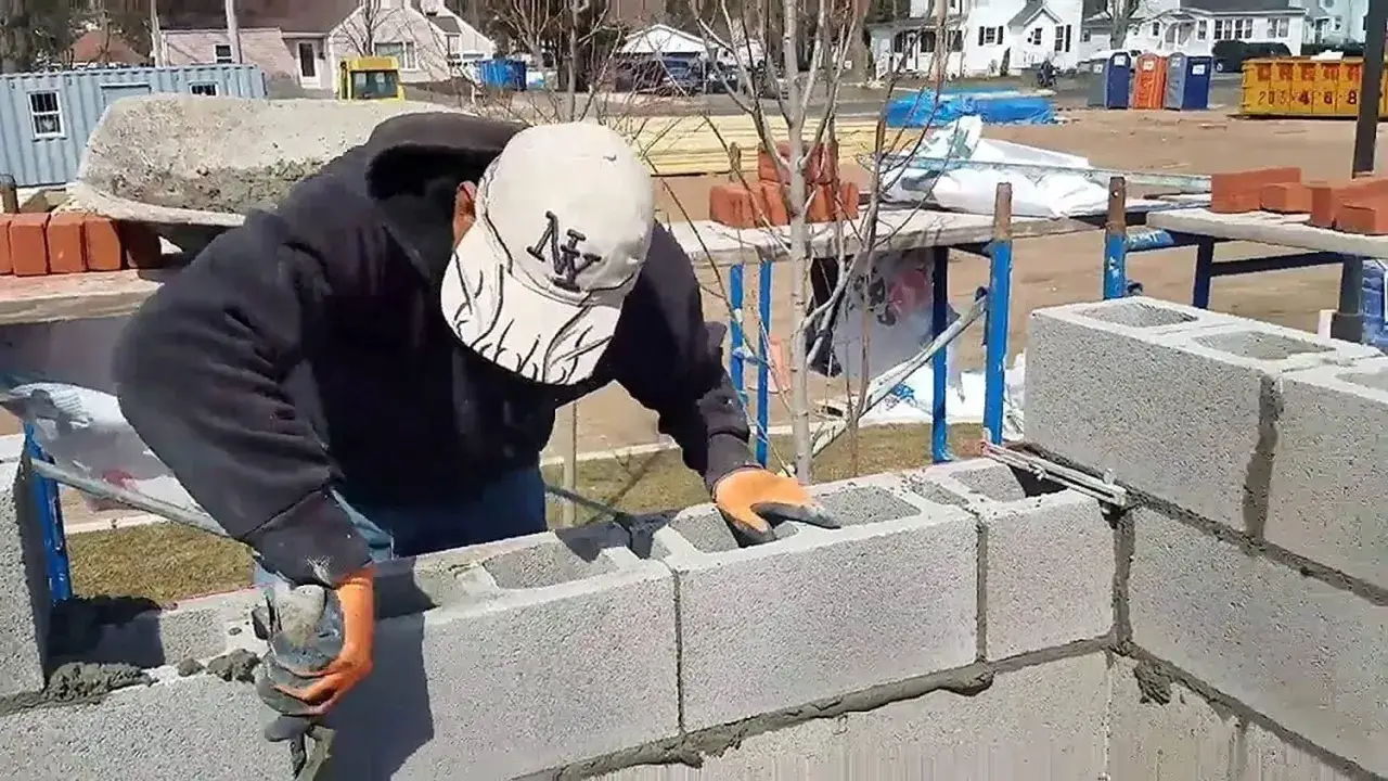 Albañil mezcla cemento y agua para construir un muro de bloques.